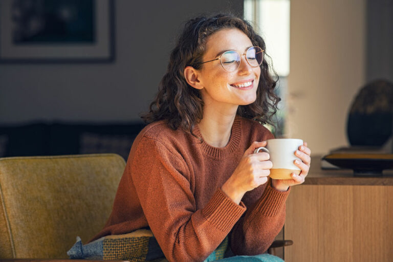 woman smiling while clutching a cup of coffee